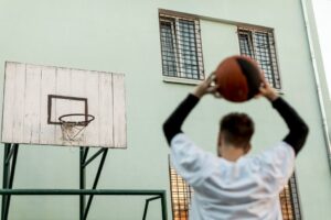 Joven jugador de baloncesto sosteniendo el balón sobre su cabeza, listo para lanzar hacia una canasta de madera en una cancha urbana al aire libre